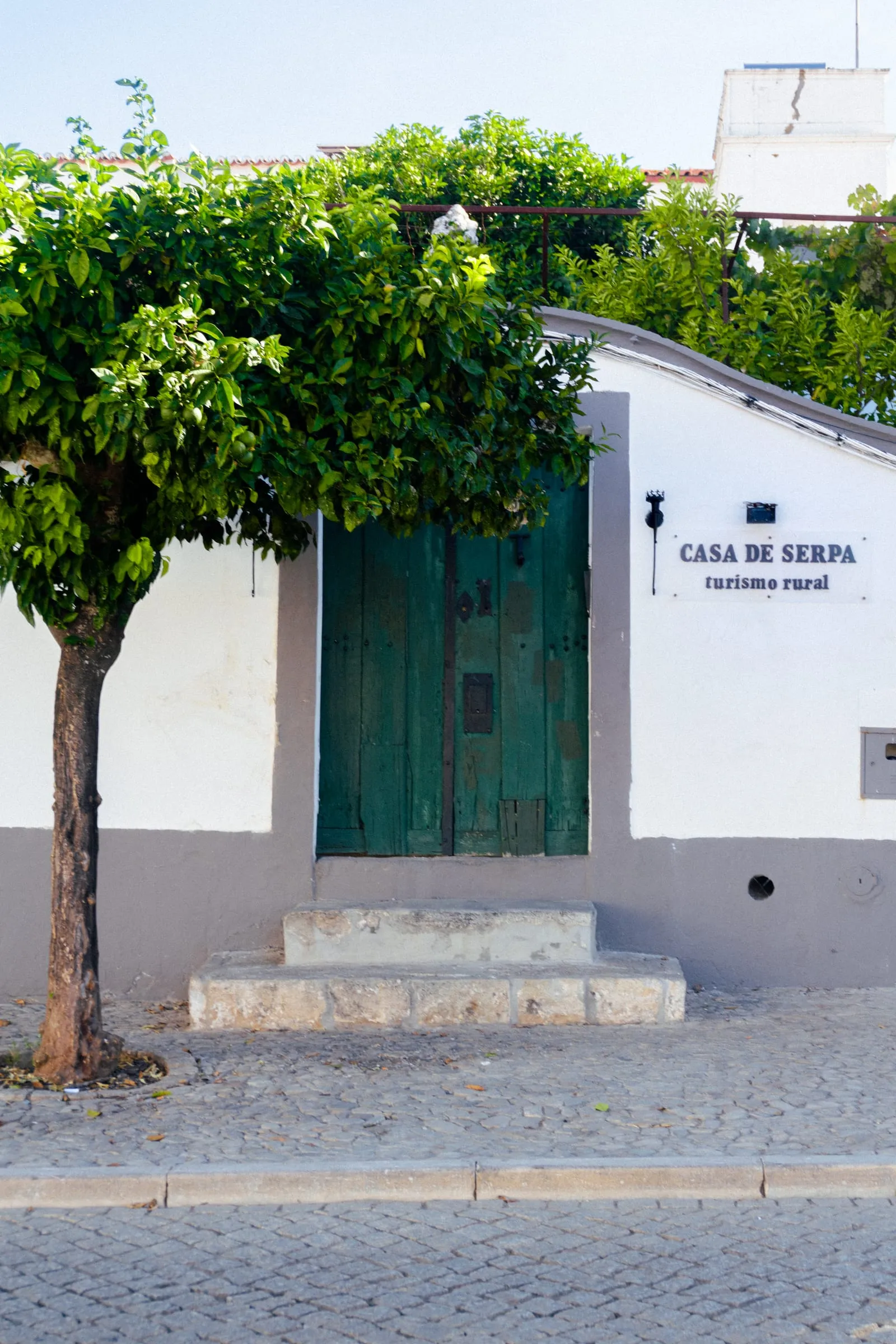 Porta verde da entrada da Casa de Serpa junto a uma laranjeira, com a placa turismo rural